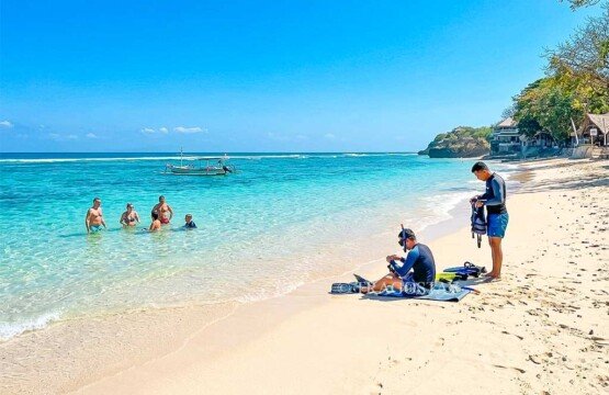 Two tourists preparing their snorkeling gear on the beach at Mushroom Bay during a sunny day.