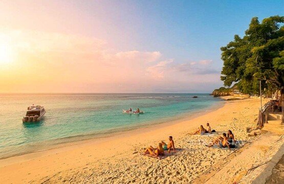 Several travelers sitting on the white sand of Mushroom Bay while watching a clear and vibrant sunset.
