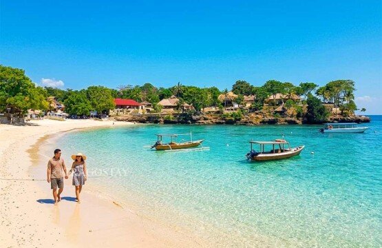 Two tourists walking on the edge of the beach at Mushroom Bay with crystal clear water and white sand.