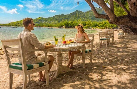 An international tourist couple smiling while enjoying a delicious lunch at an outdoor restaurant table right beside Pemuteran Beach.
