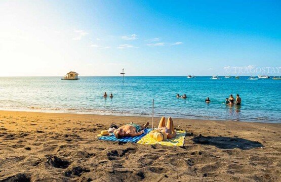 International tourists enjoying a bright sunny day at Pemuteran Beach by sunbathing on the sand and swimming in the calm ocean water.