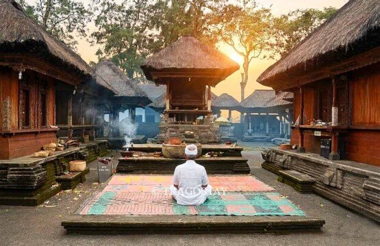 A Balinese Hindu priest in white robes ringing a bell and performing sacred morning puja prayers in the main area of Puncak Penulisan Temple.