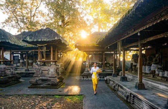 A Balinese Hindu woman holding a colorful Canang Sari floral offering in her hands inside the main compound of Puncak Penulisan Temple.