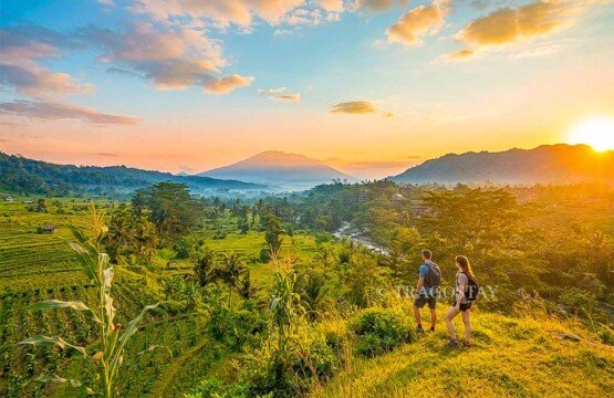 Two tourists preparing for a trekking adventure in Sidemen Rice Terrace with sunrise views of the valley and volcano.