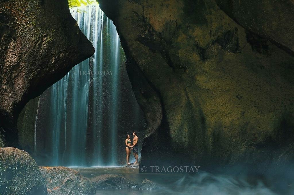 A romantic couple posing together directly under the cascading water inside the Tukad Cepung cave temple canyon.