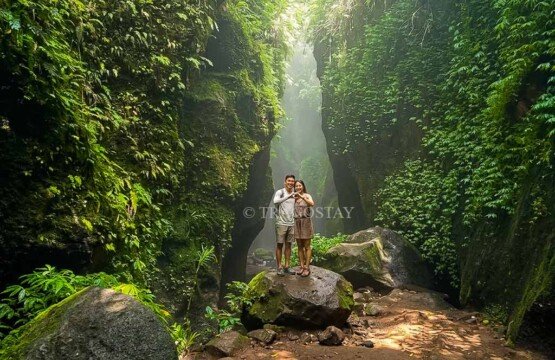 A pair of travelers posing together on a river rock wedged between the high canyon walls of Tukad Cepung.
