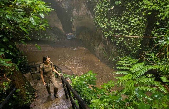 A female traveler climbing up the rustic wooden and stone steps along the canyon trail at Tukad Cepung Waterfall.