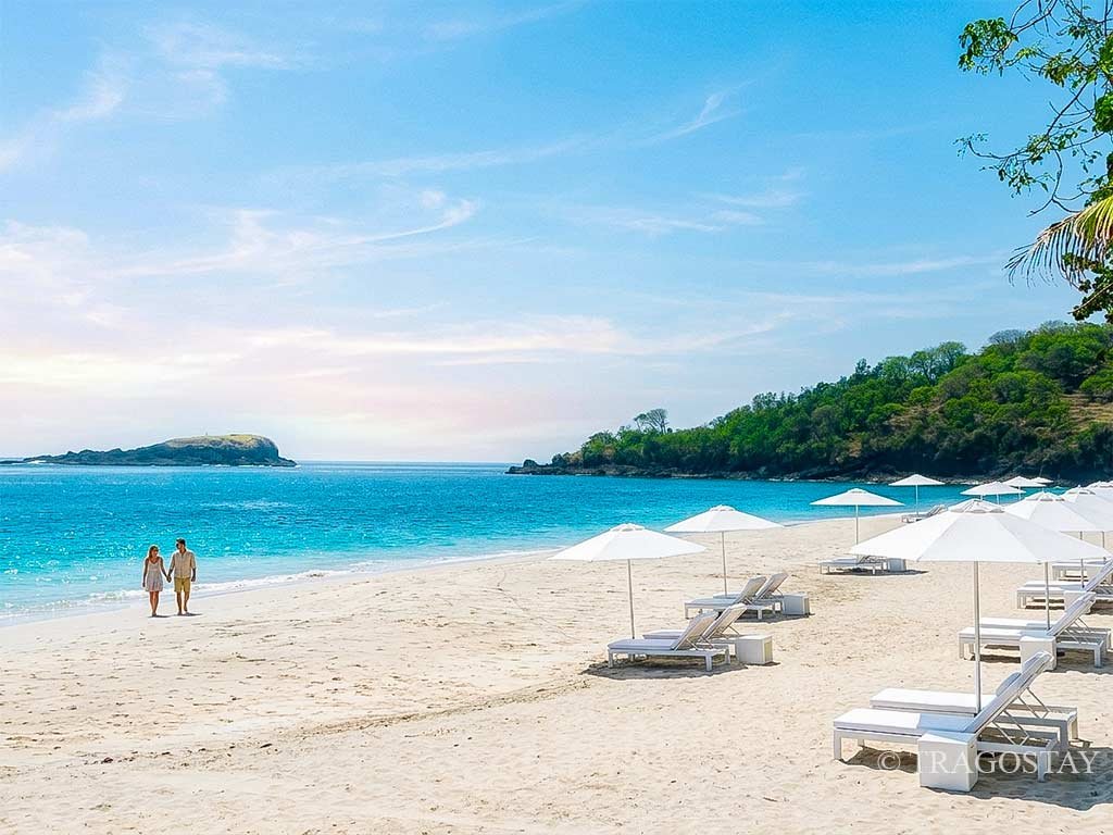White sunbeds lined up on the shore of Virgin Beach with crystal clear blue paradise water.
