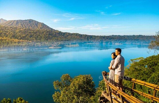 An adventurous traveling couple posing together on an overhanging wooden deck at Wanagiri Hidden Hills with a majestic mountain view.