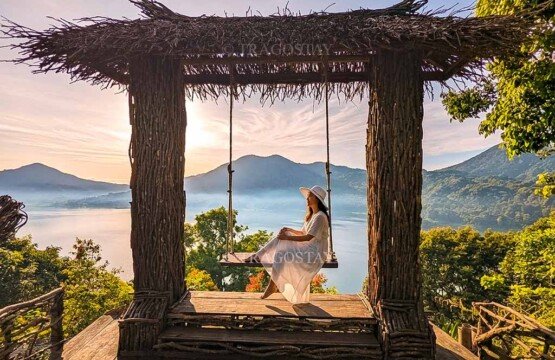 A female traveler sitting and posing on a rope swing set inside a Balinese-style wooden entrance gate at Wanagiri Hidden Hills in the morning.