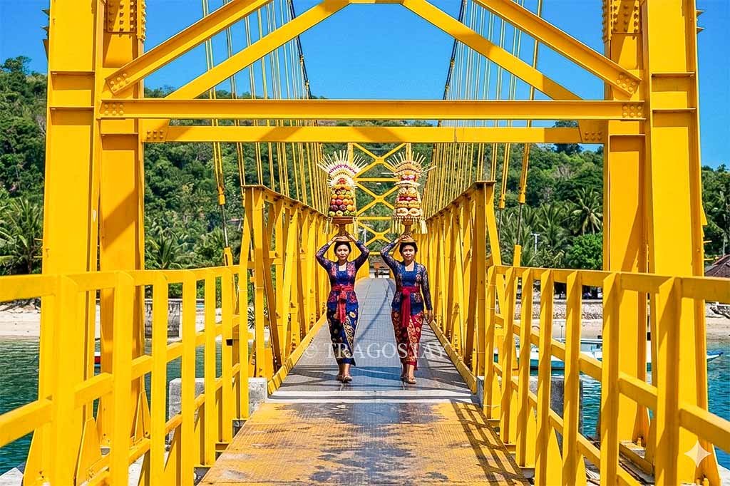 Two Balinese girls in traditional attire carrying Gebogan offerings while walking across the Yellow Bridge.