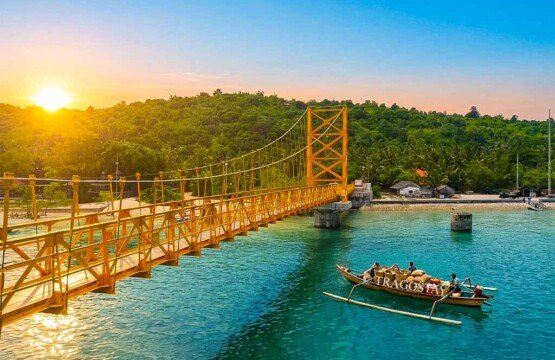 A traditional fishing boat loaded with supplies sailing underneath the Yellow Bridge in the morning sun.