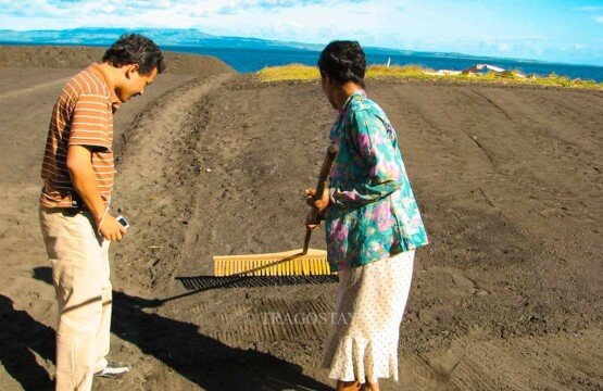 A Balinese female salt farmer demonstrating how to evenly spray seawater on the sand to tourists at Kusamba Beach.